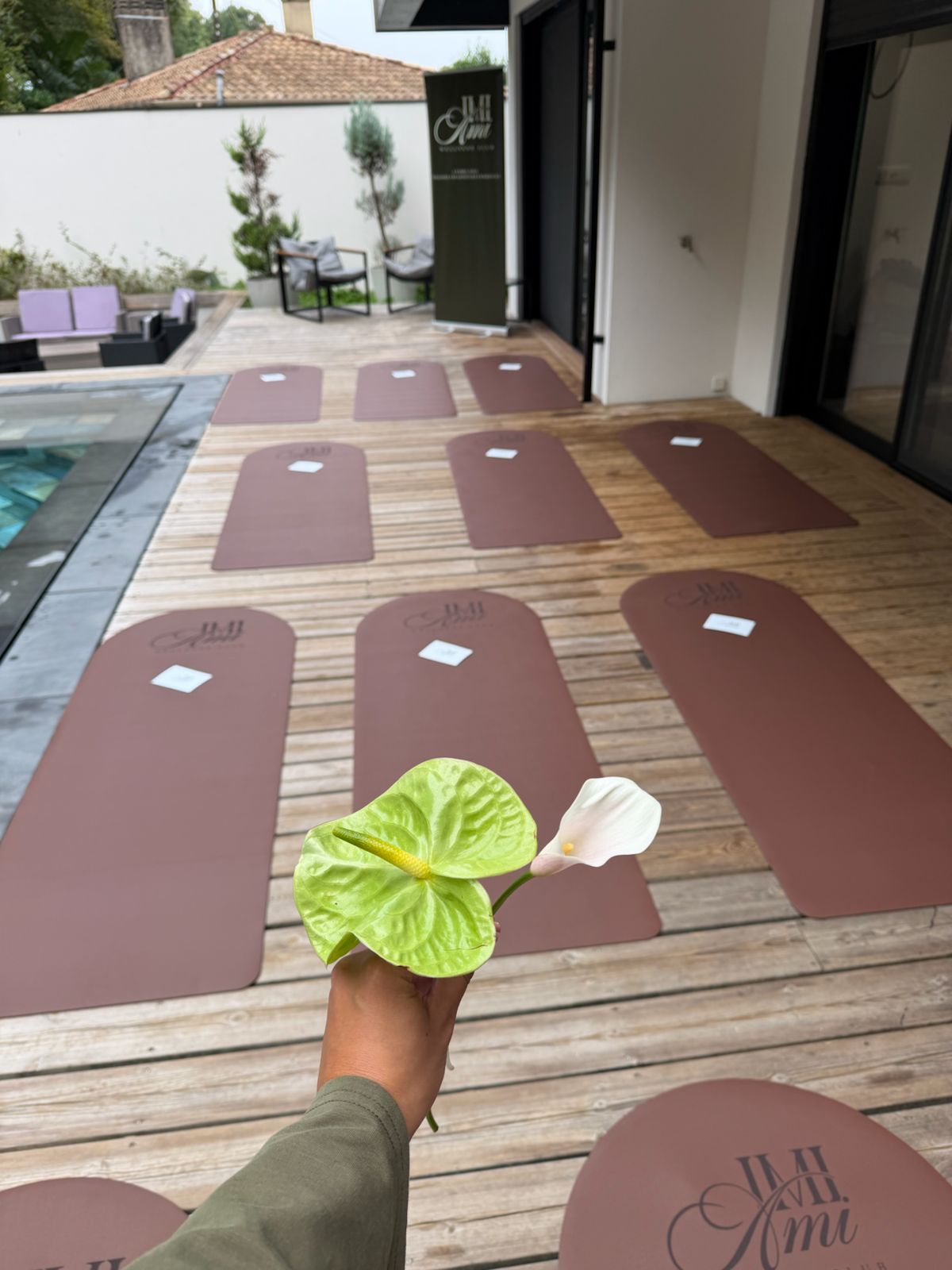 Une main tient un anthurium vert et un arum blanc au-dessus des tapis alignés le long de la piscine.
