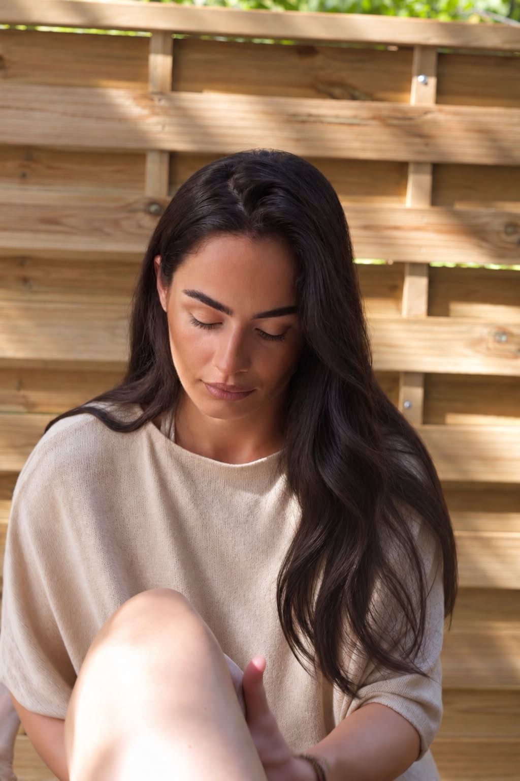 Portrait d'une participante assise, les yeux baissés, dans la lumière filtrée d'une claustra en bois.
