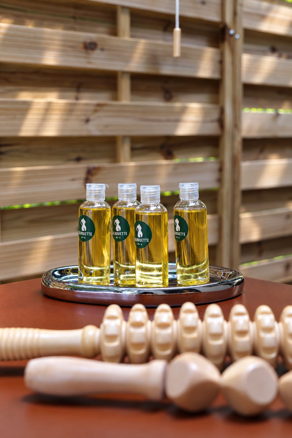 Flacons d'huile de massage alignés sur un plateau argenté, accessoires de bois au premier plan.